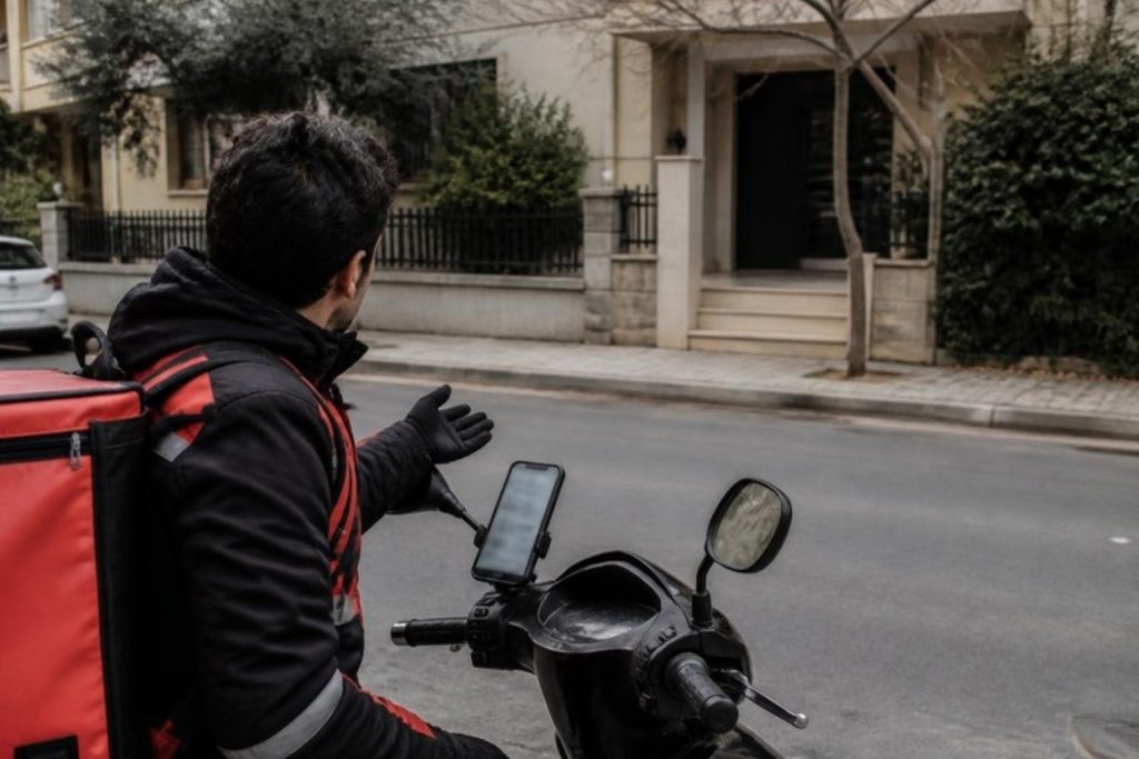 Sokak köşesinde telefondaki haritaya bakan motosikletli kurye